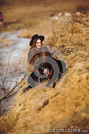 Lifestyle portrait of young woman in black hat with her dog, resting by the lake on a nice and warm autumn day Stock Photo