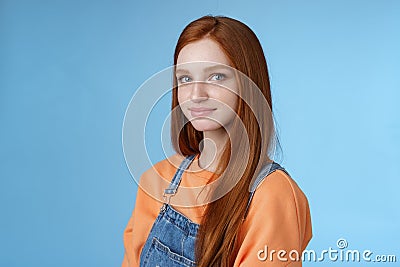 Waist-up kind sincere tender lovely redhead girl wearing orange shirt denim overalls standing half-turned smiling silly Stock Photo