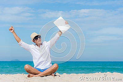 Lifestyle young asian man relaxing after working on laptop while sitting on the beautiful beach, freelance working on holiday summ Stock Photo