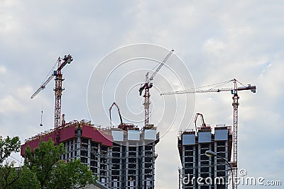 Lift tower cranes on construction site against background of the blue sky, houses new buildings near a residential area Stock Photo