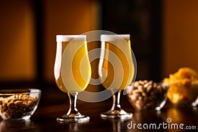 Light ale with snacks. Glasses of beer with nuts, pistachios and chips in plates on wooden table Stock Photo