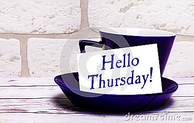 On a light background, a blue cup with a saucer and the inscription HELLO THURSDAY Stock Photo