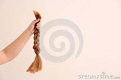 Female hand with braided strand on light background. Concept of hair donation Stock Photo