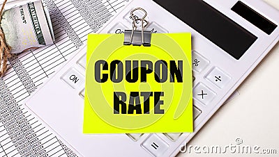 On a light background - cash, a white calculator and a yellow sticker under a black paper clip with the text COUPON RATE. Business Stock Photo