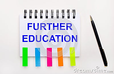 On a light background, a pen, a notebook with the text FURTHER EDUCATION and bright stickers Stock Photo