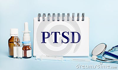 On a light background, a syringe, a stethoscope, vials of medicine, an ampoule and a white notepad with the text PTSD. Medical Stock Photo