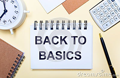 On a light background, a white alarm clock, a calculator, a pen and a notebook with the text BACK TO BASIC Stock Photo