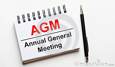On a light background, a white notebook with are words AGM Annual General Meeting and a pen Stock Photo