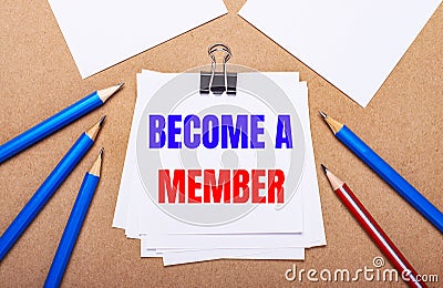 On a light brown background, blue and red pencils and white paper with the text BECOME A MEMBER Stock Photo