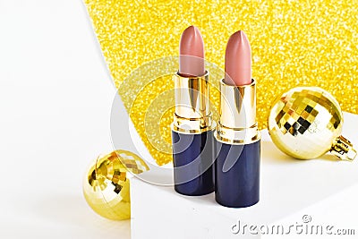 Light brown lipsticks on a shiny yellow background with Christmas golden balls . Christmas gift for women. Festive decoration of c Stock Photo