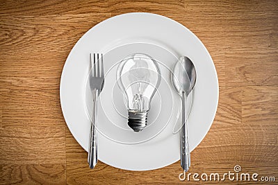 Light bulb in plate and fork and spoon on wooden table Stock Photo