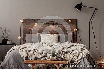 Light bulbs on wooden headboard of comfortable bed with grey bedding and warm fury blanket Stock Photo