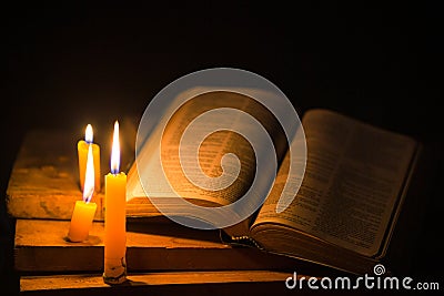 Light candle with holy bible and cross or crucifix on old wooden background in church.Candlelight and open book on vintage wood Stock Photo