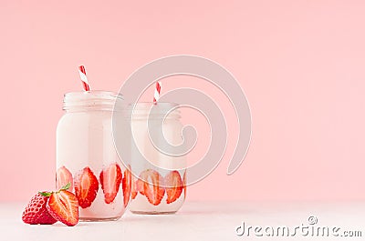 Light dairy strawberry drinks in trendy jars with ripe pieces berries, red striped straws on gentle pink background and white wood Stock Photo