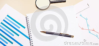 On a light desktop, charts and reports, a magnifying glass, a pen and a blank notepad to insert text. Template. Top view with copy Stock Photo