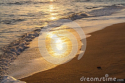 Golden shimmering sunset light on gentle waves on a sandy beach Stock Photo