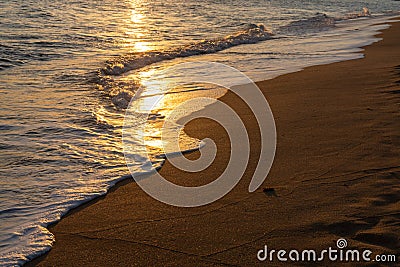 Golden shimmering sunset light on gentle waves on a sandy beach Stock Photo
