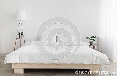 Light minimalist design in bedroom interior. Double bed with white pillows and blanket, lamp, white wall , copy space Stock Photo