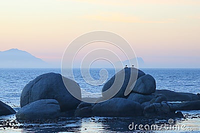 Large boulders at sea with birds and hazy sunrise Stock Photo
