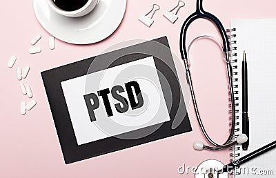 On a light pink background, a notebook with a pen, stethoscope, white pills, paper clips and a sheet of paper with the text PTSD. Stock Photo