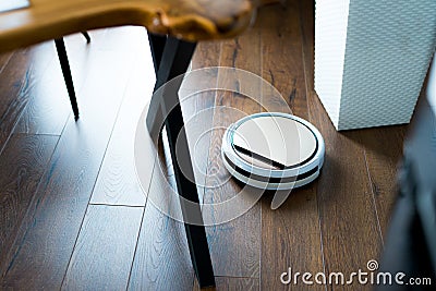 Light robot vacuum cleaner removes dust and dirt in an apartment on a wooden parquet Stock Photo