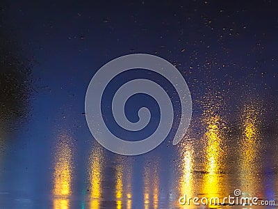 Light from shop Windows is reflected on the wet asphalt. View from the asphalt level. Background Stock Photo