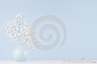 Light soft elegant home decor with small airy flowers in glossy pastel blue vase on wood table and blue wall. Stock Photo