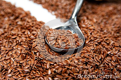 A light stone with a dark gray metal spoon on it lies against a background of brown flax seeds. Stock Photo