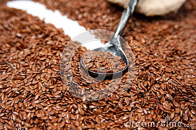 Dark grey metal spoon lies against a background of brown flax seeds. On a spoon are flax seeds Stock Photo