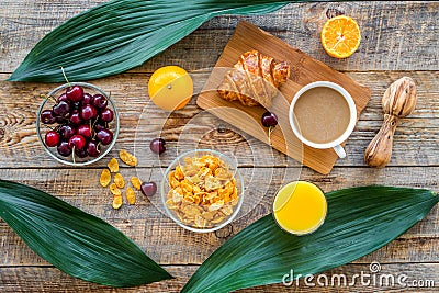 Light tasty breakfast. Muesli, oranges, cherry, french croissant and milky coffee on wooden table background top view Stock Photo