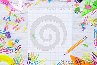 Light wooden background with colored pencils on the sides of the clipped notebook, there is a place for writing in the middle. Stock Photo
