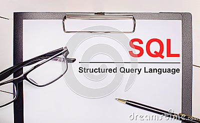 On a light wooden background glasses, a pen and a sheet of paper with the text SQL Structured Query Language. Business concept Stock Photo