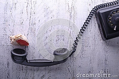 On a light worn wooden table stands a vintage black telephone with a handset removed from the lever. Stock Photo