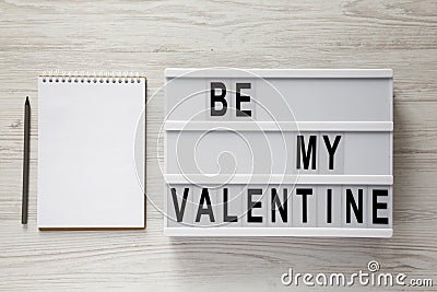 Lightbox with text `Be my Valentine`, blank notepad over white wooden surface. Valentine Day 14 February Stock Photo