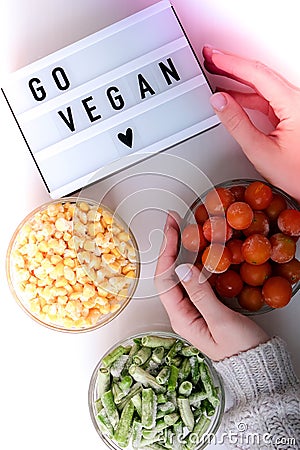 Lightbox with text GO VEGAN Three Bowls of frozen vegetables food of yellow corn, green beans, red tomatoes. Colors of traffic Stock Photo