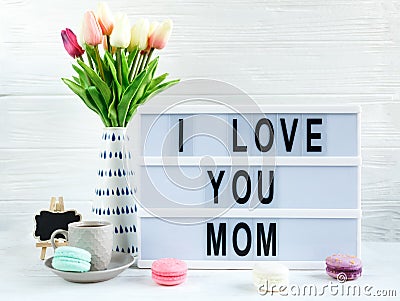 Lightbox with title Ilove you mom and tender tulips, macaroons on white wooden background. Mothers day decoration concept. Stock Photo