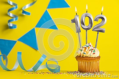 Lighted birthday candle number 102 - Yellow background with blue pennants Stock Photo