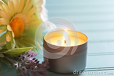 Lighted and Scented votive Candle in a tin holder with flowers on the side, all on teal boards table background with window light Stock Photo