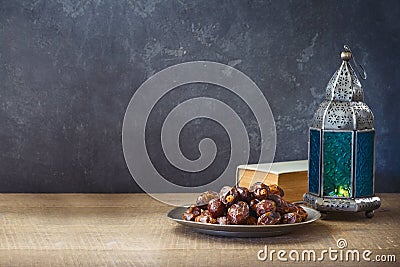 Lightened lantern and dates fruit on wooden table over dark background. Ramadan kareem holiday celebration concept Stock Photo