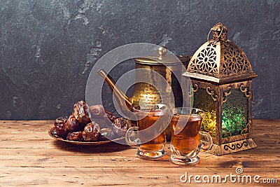 Lightened lantern, tea cups and dates on wooden table over blackboard background. Ramadan kareem holiday celebration Stock Photo