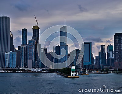 Lighthouse juts into Lake Michigan with marina of sailboats on left, loch on right, and skyline of Chicago with evening sunset in Editorial Stock Photo