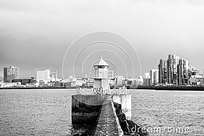 Lighthouse in reykjavik, iceland. Lighthouse tower and stone pier in sea. Seascape and skyline on grey sky. Architecture Stock Photo
