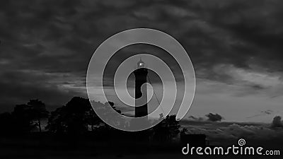 Lighthouse shines in the dark with a dramatic sky. silhouette of glowing beacon in darkness Stock Photo