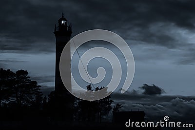 Lighthouse shines in the dark with a dramatic sky. silhouette of glowing beacon in darkness Stock Photo