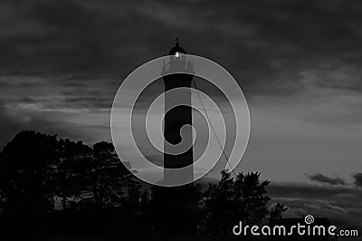 Lighthouse shines in the dark with a dramatic sky. silhouette of glowing beacon in darkness Stock Photo