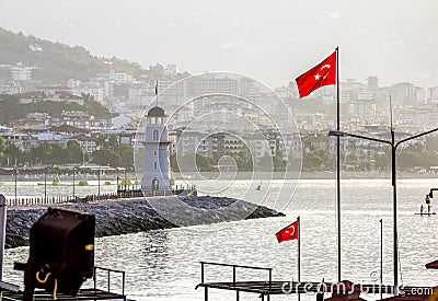 Lighthouse and Turkish flags in the Harbor in Alanya in Turkey at dawn Stock Photo
