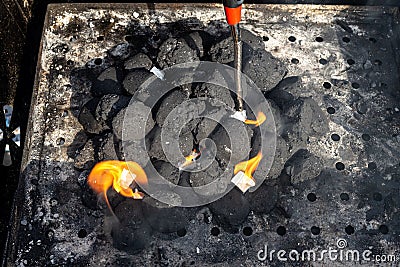 Lighting a home grill with charcoal and white kindling for the grill, standing in the home garden, using a barbecue lighter. Stock Photo