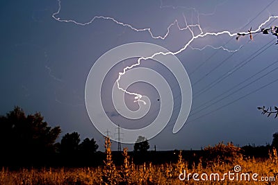 Lightning fast on a stormy summer night. A field with poles and electric wires Stock Photo