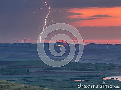 Lightning in the sunset sky over the hills with wind turbines and lake Stock Photo