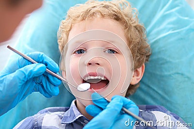 Liittle curly boy opening his mouth wide during inspection of oral cavity by dentist. Stock Photo